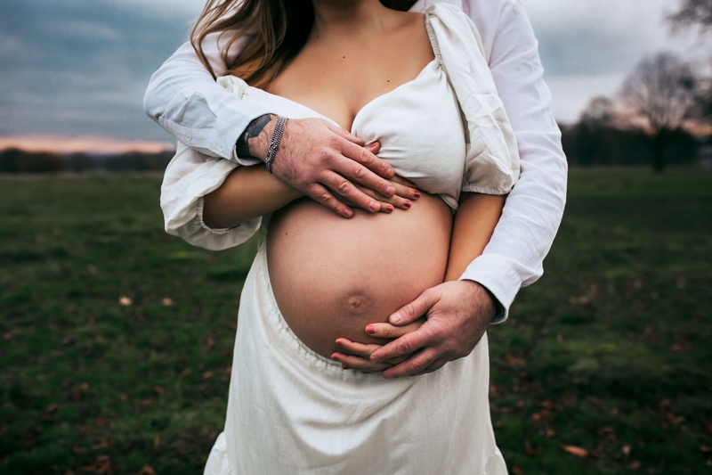 London Family Photographer, a man and woman's hands embrace a pregnant belly outdoors