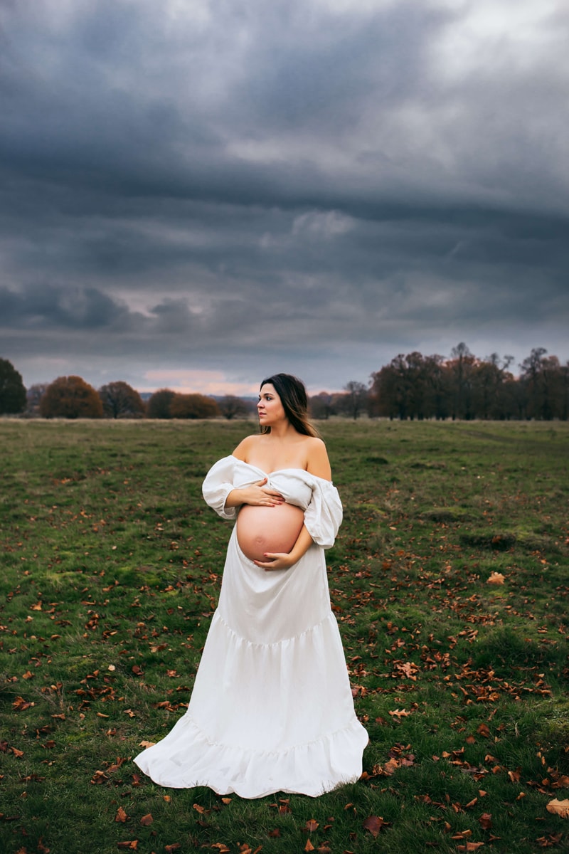 London Family Photographer, an expecting mother lovingly holds her hands on her belly outside