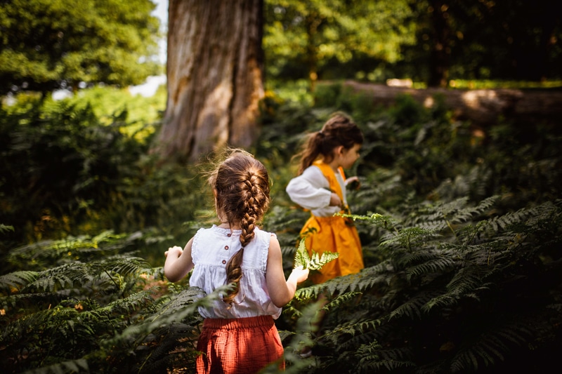 London Family Photographer, two young girls navigate through ferns in the forest, they are happy exploring