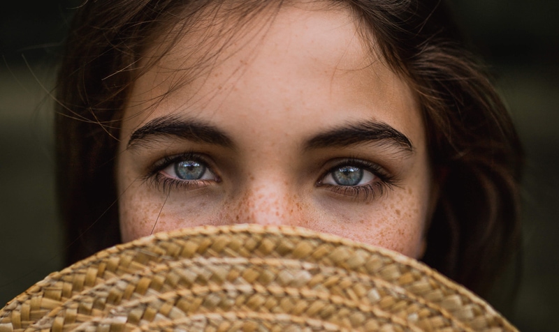 London Family Photographer, a young woman pokes her blue eyes out from behind a straw hat hiding her face