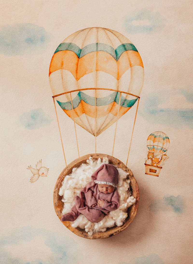 London Family Photographer, a baby lays sleeping a round basket, the floor beneath is painted with a hot air balloon, as if baby was floating away